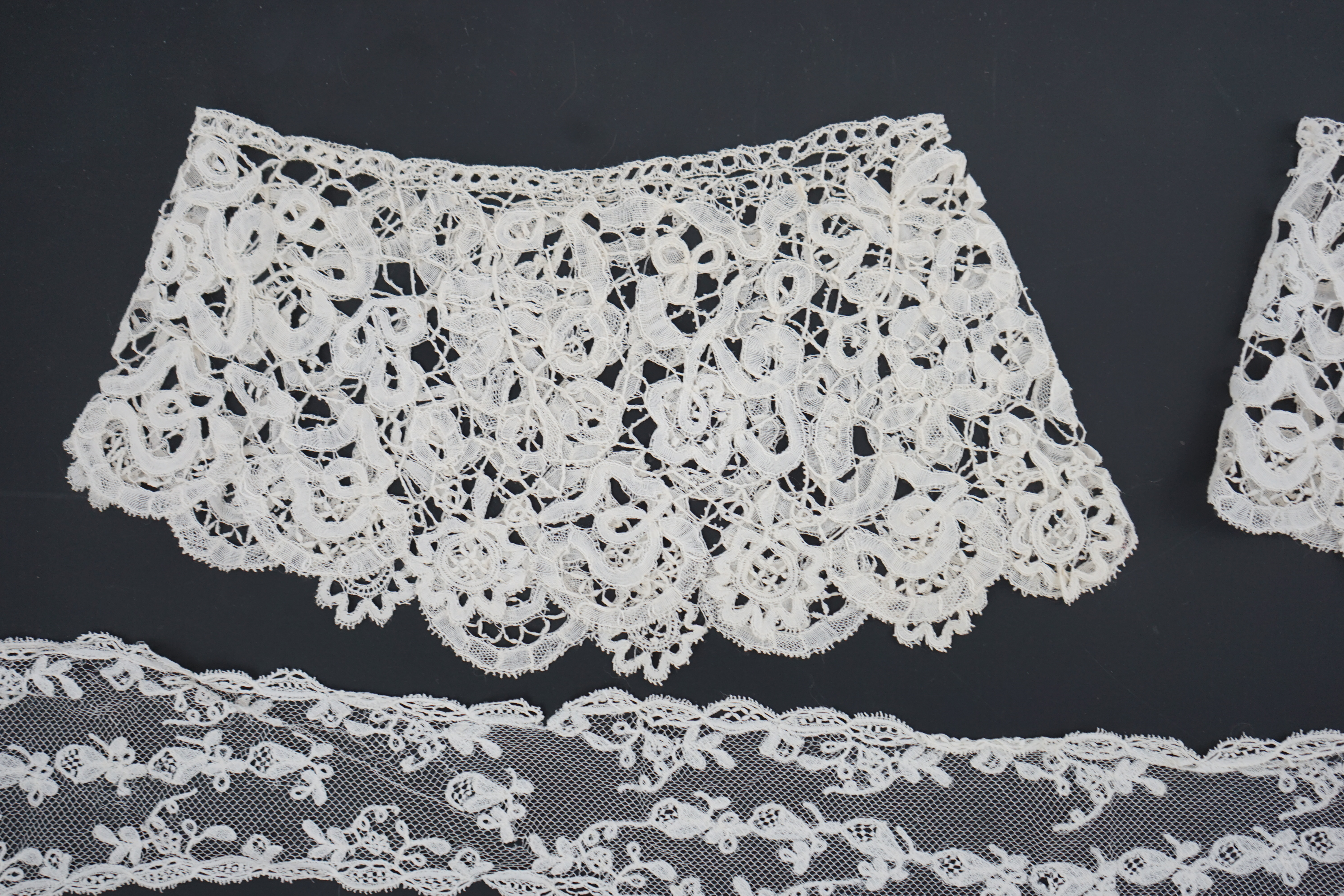 A small collection of late 19th century laces including a cream Brussels bobbin lace collar appliquéd on to net and two similar Brussels bobbin lace lappets, a pair of cream Honiton bobbin lace cuffs and a black lace fal